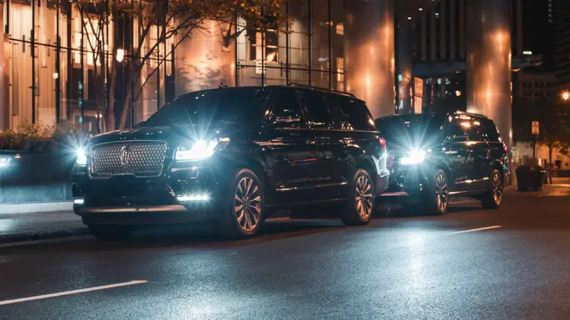 Black executive SUVs at the curb outside a Chicago office tower at night